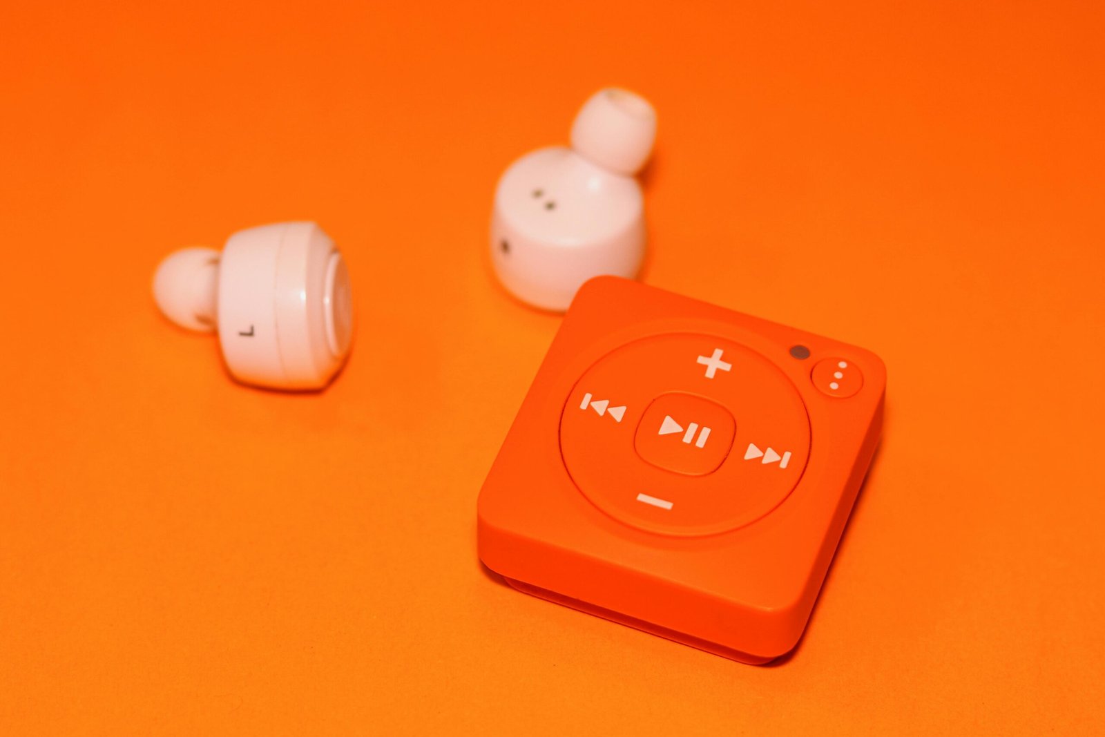 Close-up of wireless earphones and a compact music player on an orange background, showcasing modern audio technology.